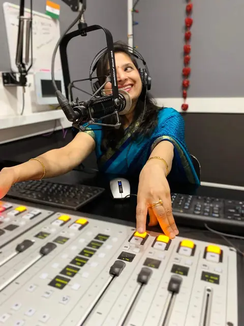 Swati at the studio mixing desk, smiling into the microphone
