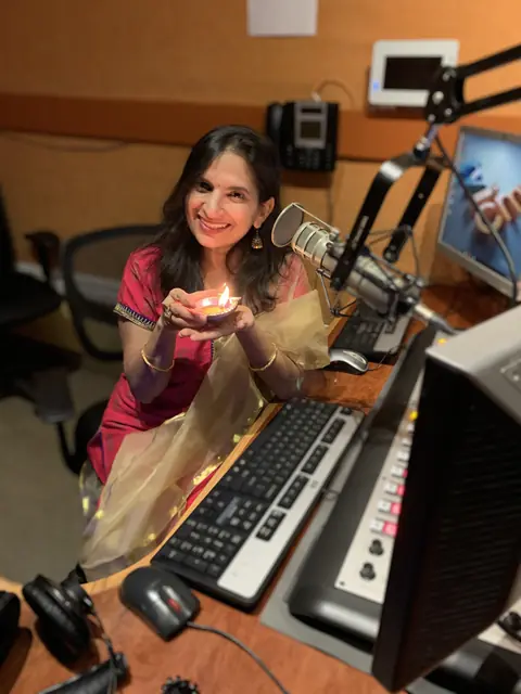 Swati holding a lit diya at the studio console