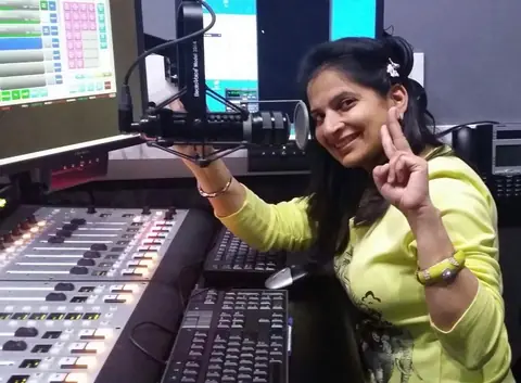Swati making a peace sign beside the broadcast console